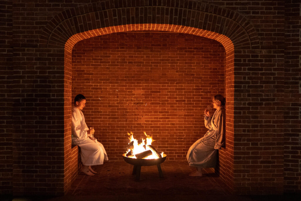 Guests beside a fire pit in a brick alcove at night