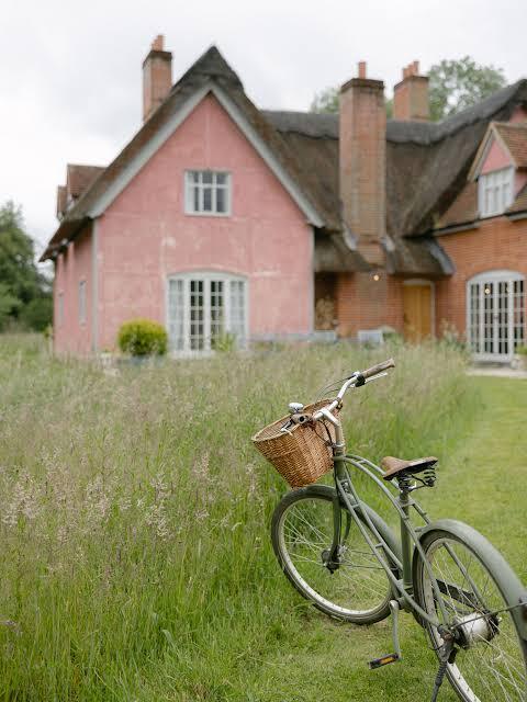 Pink thatched estate cottage with a bicycle in the long meadow grass